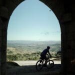 A Slow Cyclist riding through an arch in Portugal's Douro region with mountains in the background.