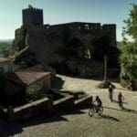 Three Slow Cyclists riding on a cobbled road in a traditional Portuguese village near the Coa river with a castle in the background.