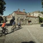 Three Slow Cyclists riding through a traditional Portuguese stone village near the Coa river.