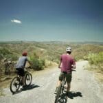 Two Slow Cyclists pausing on their bikes to look over the hills of the Douro region, Portugal.